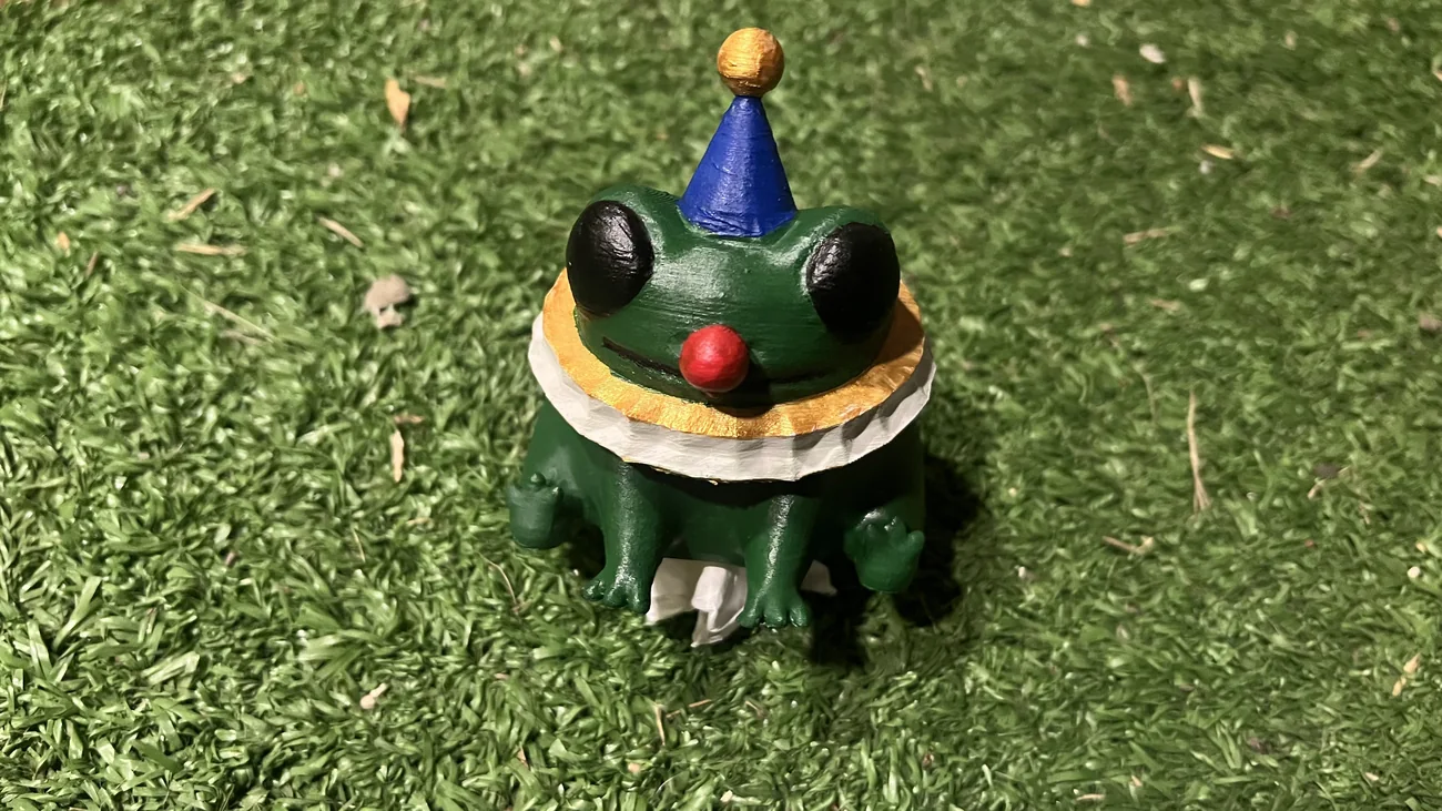 Figura verde con sombrero azul y nariz roja, fotografiada sobre césped