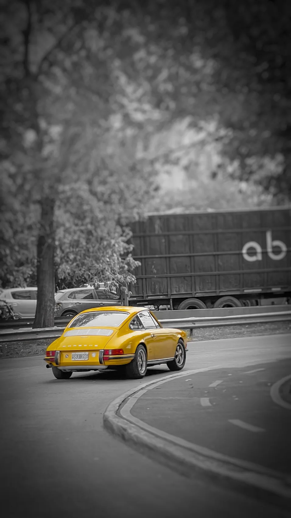 Porsche amarillo en una curva, con el entorno en blanco y negro