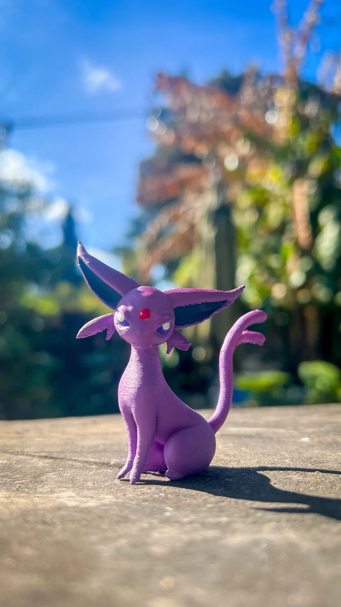 Figura Espeon violeta fotografiada al aire libre, toma editada con color más saturado